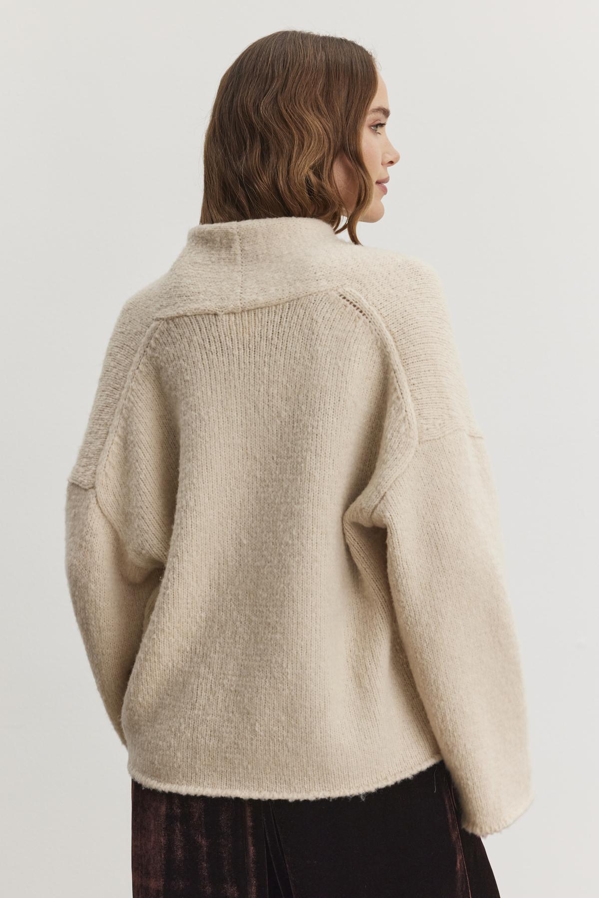   The individual is enveloped in the CHANSON CARDIGAN, an oversized beige knitted sweater featuring a shawl collar, by Velvet by Graham & Spencer, facing away. 