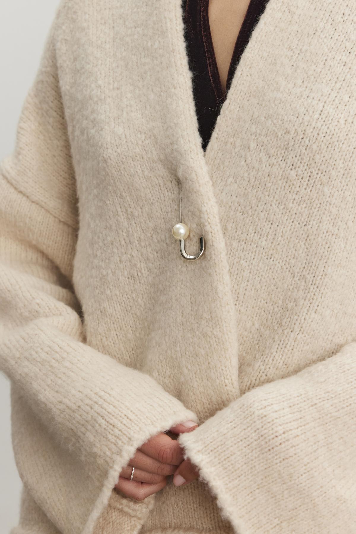   A person wearing the CHANSON CARDIGAN by Velvet by Graham & Spencer, a beige wool blend sweater with a pearl hook clasp and a shawl collar. 