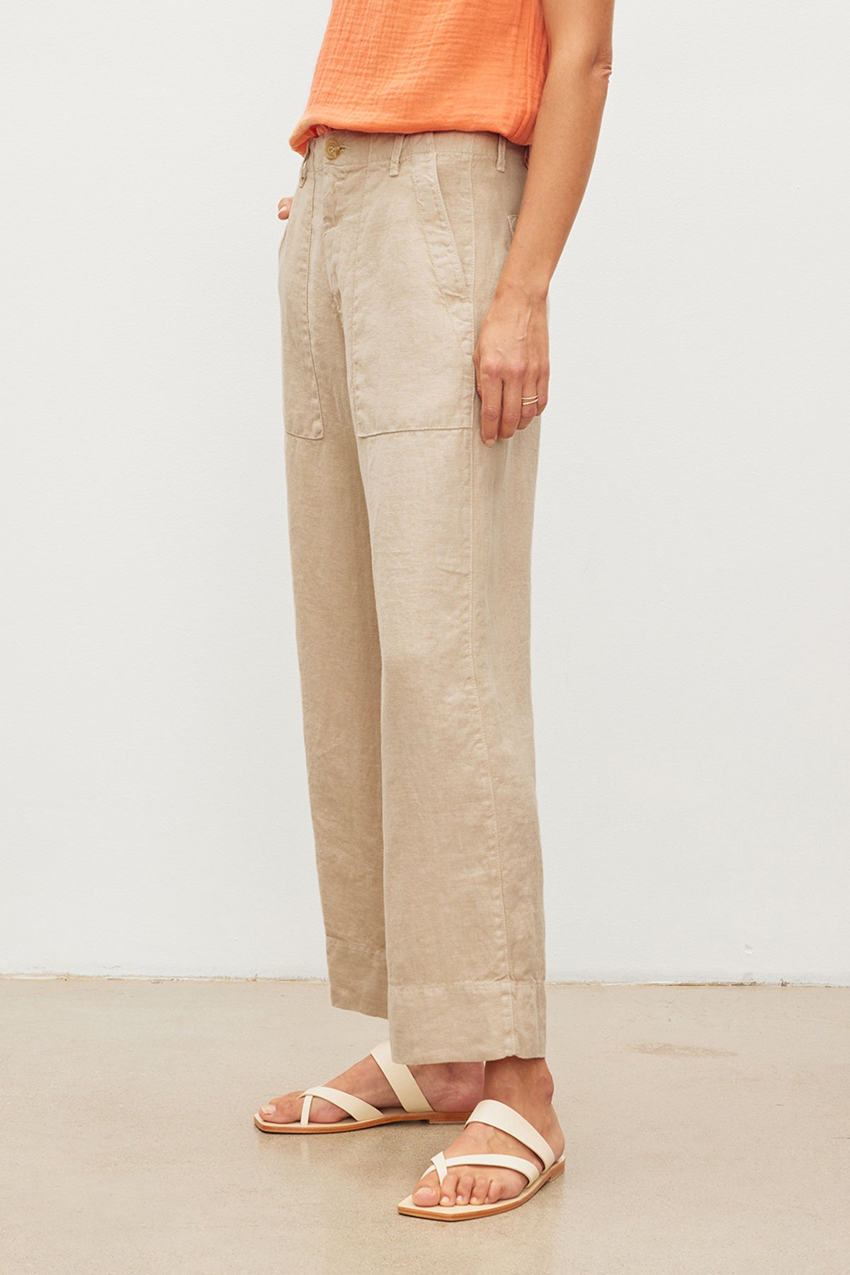   A person standing in a Velvet by Graham & Spencer DRU HEAVY LINEN PANT with patch pockets and white sandals against a plain background. 