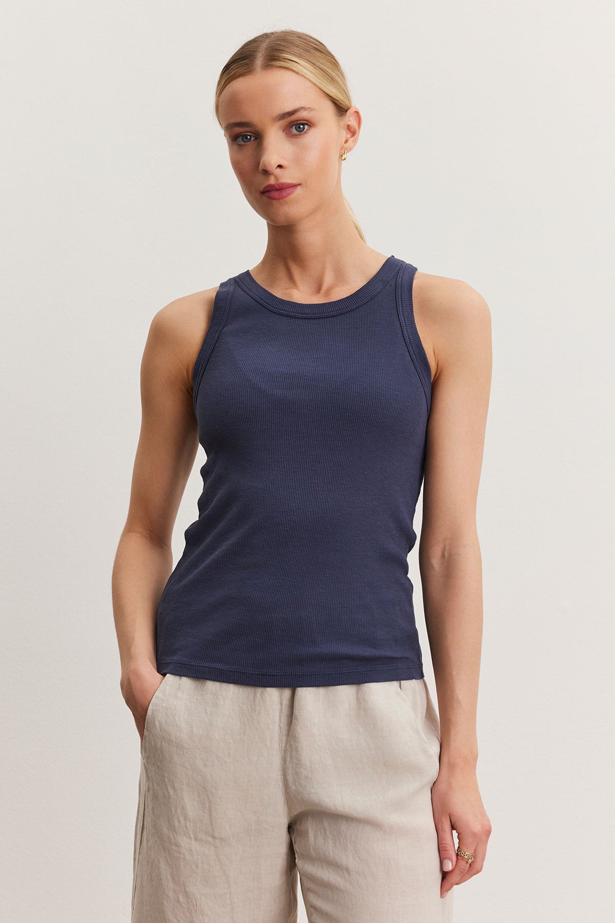 A woman in a navy blue Velvet by Graham & Spencer NOLA tank top and beige pants standing against a plain background.-36998713442497