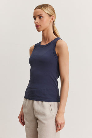 A woman wearing a fitted Velvet by Graham & Spencer NOLA tank top and beige trousers stands against a light background, looking to the side.