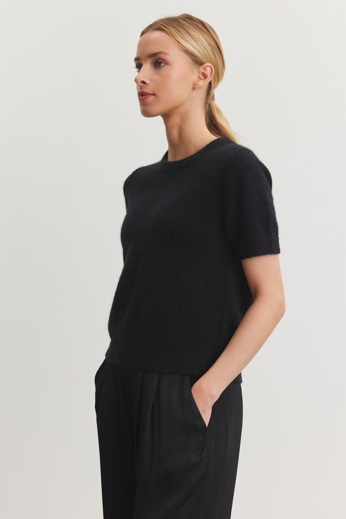 A person with blonde hair tied back is wearing the LAYTON ALPACA SWEATER by Velvet by Graham & Spencer, paired with black pants, standing against a plain white background.-38246577799361