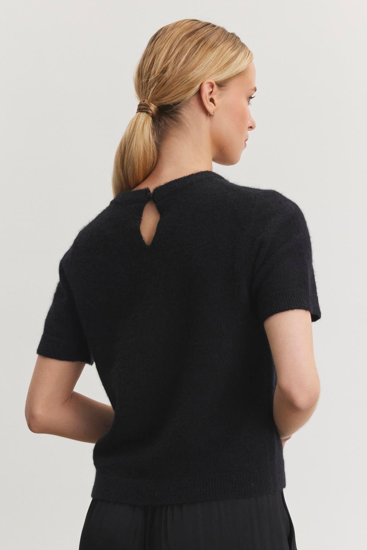   A person with blonde hair in a ponytail is shown from the back wearing the LAYTON ALPACA SWEATER by Velvet by Graham & Spencer, which features short sleeves and a small back keyhole detail. 