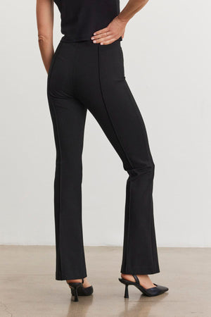 A person wearing the ALBEE PONTE PANT by Velvet by Graham & Spencer, which features a boot-cut silhouette, and black heels stands with their hand on their hip, facing away from the camera.