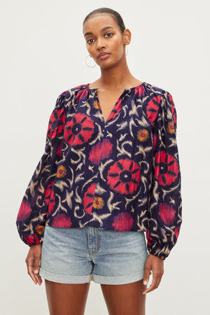 Woman posing in a Fraser printed silk cotton voile top by Velvet by Graham & Spencer with long sleeves and an elastic neckline, paired with denim shorts.