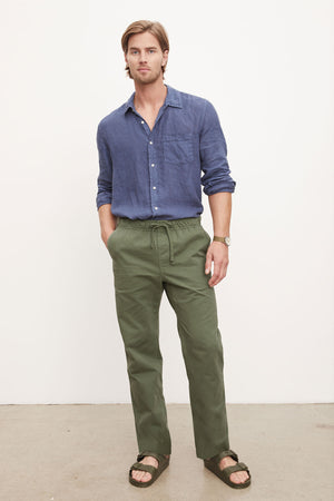 Man in a blue shirt and green BRANSON PANT by Velvet by Graham & Spencer with an elastic drawstring waist posing for a photo.