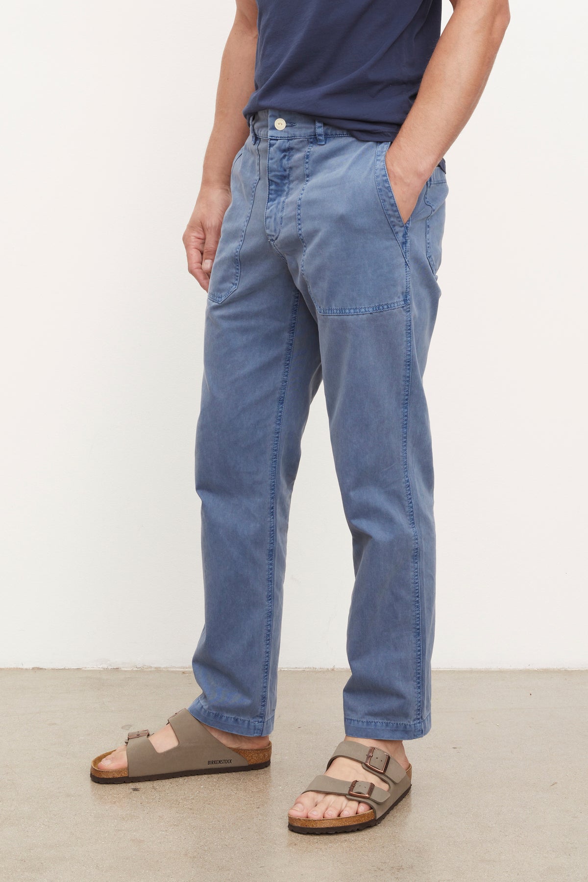   A man wearing Velvet by Graham & Spencer's TOBY SANDED TWILL PANT and sandals standing in front of a white wall. 