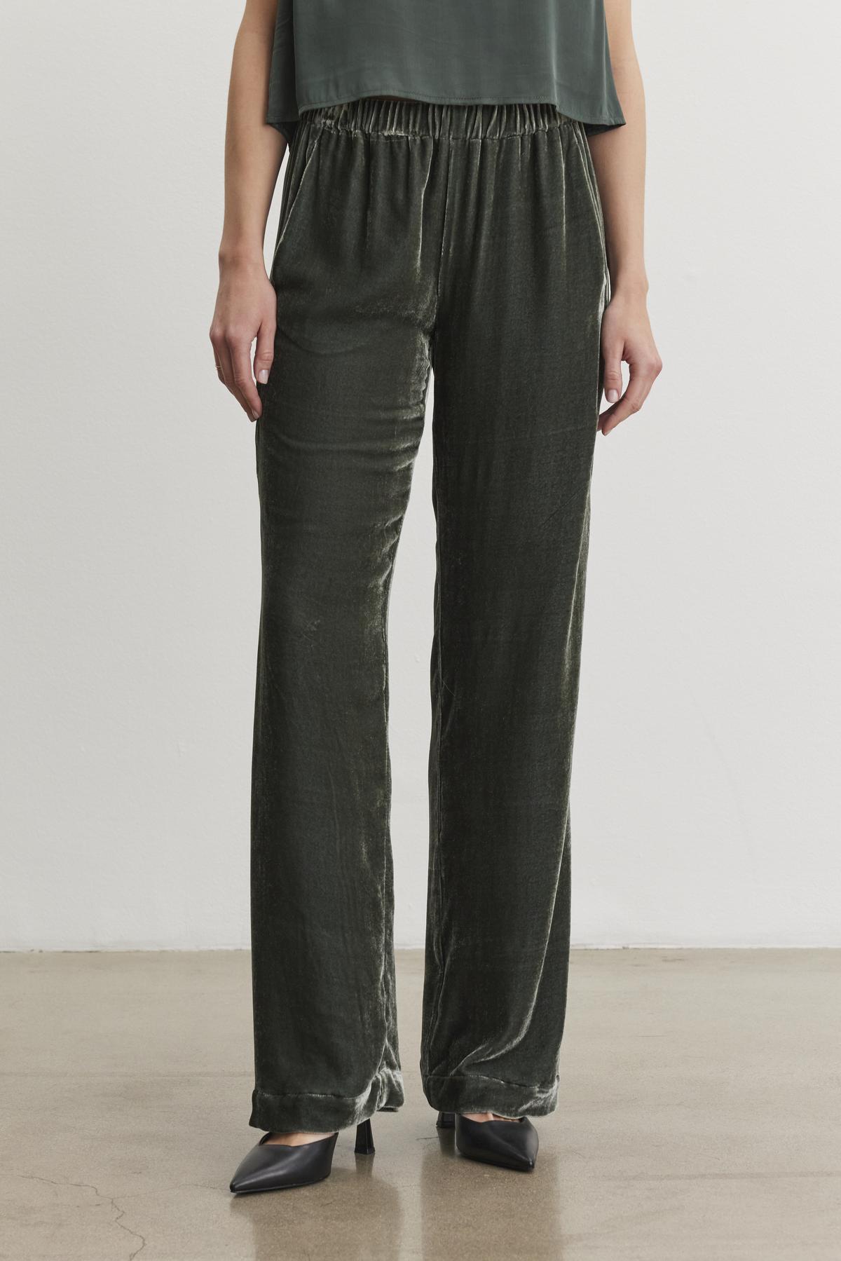 An individual in the SORINE SILK VELVET PANT by Velvet by Graham & Spencer, paired with black pointed shoes, is positioned against a plain white background.-38246701629633