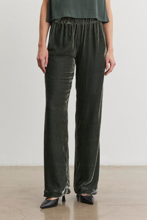 An individual in the SORINE SILK VELVET PANT by Velvet by Graham & Spencer, paired with black pointed shoes, is positioned against a plain white background.