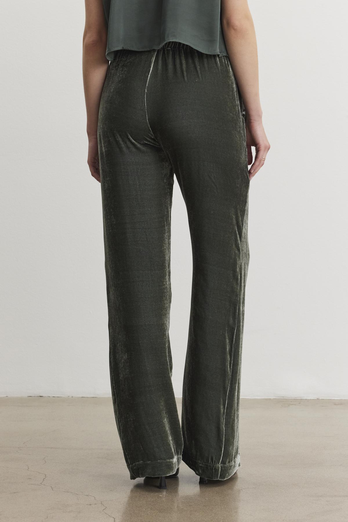   A person wearing the SORINE SILK VELVET PANT by Velvet by Graham & Spencer, along with a matching top, is viewed from the back while standing on a polished floor. 