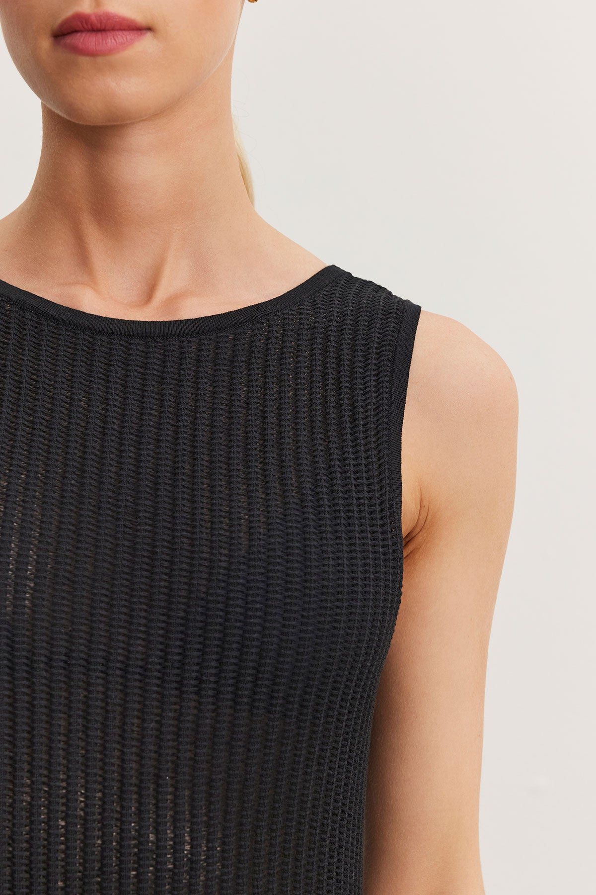 Close-up of a woman wearing a ribbed black sleeveless Velvet by Graham & Spencer CALLEN DRESS, focusing on the garment's texture and her shoulder.-36998731923649