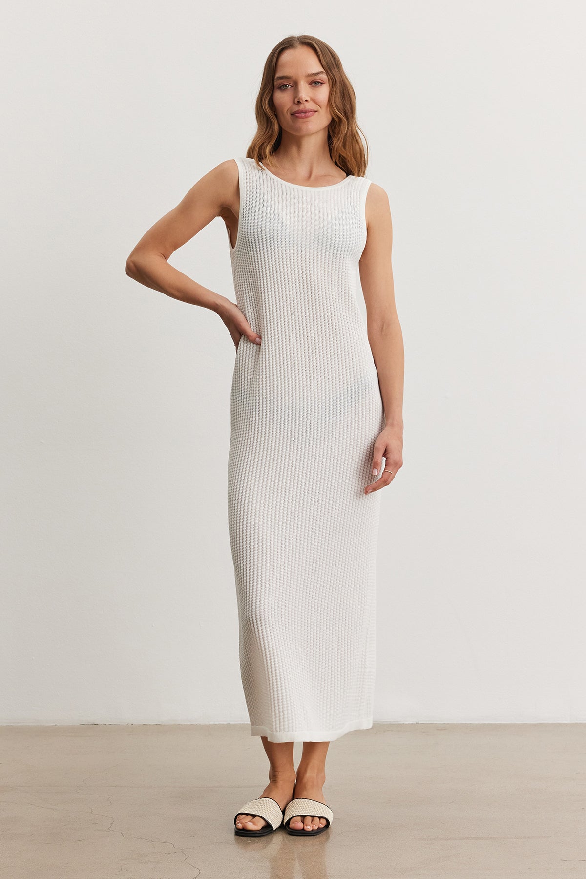   Woman in a white CALLEN DRESS by Velvet by Graham & Spencer standing with one hand on her hip in a bright, minimalistic room. 