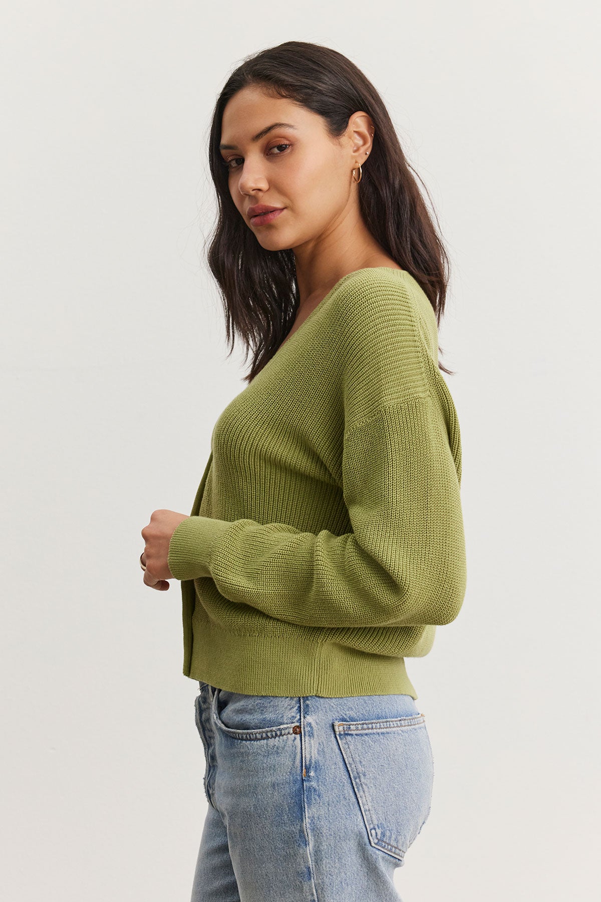   Woman wearing a Velvet by Graham & Spencer Tava cardigan and blue jeans, standing sideways and looking at the camera. 