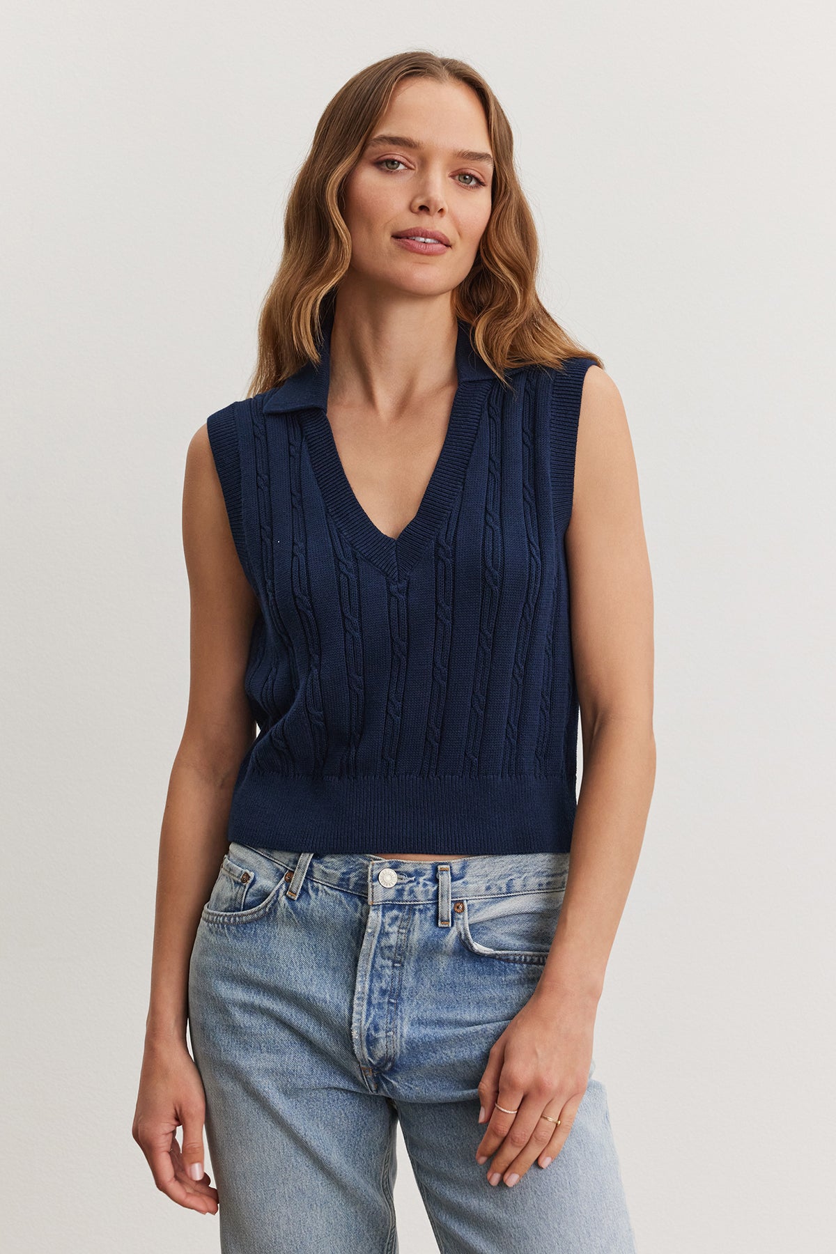   A woman wearing a navy blue WENDY SWEATER VEST and light blue jeans stands against a neutral background. Brand: Velvet by Graham & Spencer 