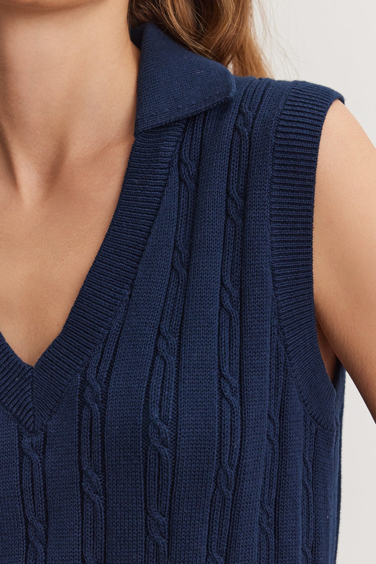   Close-up of a woman wearing a dark blue WENDY SWEATER VEST by Velvet by Graham & Spencer, with a collared shirt underneath, focusing on the detailed texture of the knit fabric. 