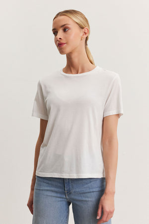 A woman in a Velvet by Graham & Spencer RYAN TEE and blue jeans standing against a white background, looking to the side.