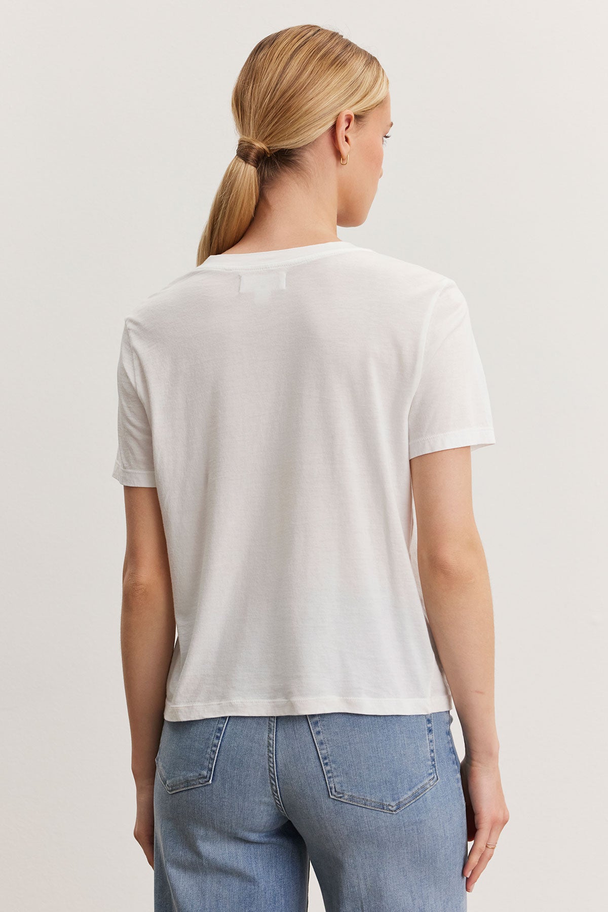   Rear view of a woman with a ponytail wearing a Velvet by Graham & Spencer RYAN TEE in whisper cotton fabric and blue jeans, standing against a light background. 