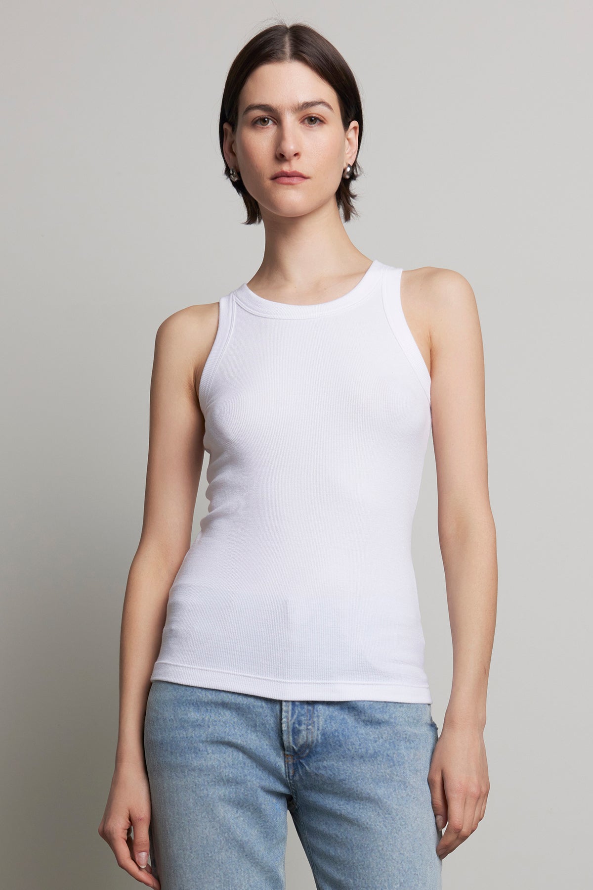 A person with short hair wearing the CRUZ TANK TOP by Velvet by Jenny Graham, crafted from ribbed cotton-modal, and blue jeans stands against a plain background, embodying the essence of a capsule wardrobe.-38318609268929