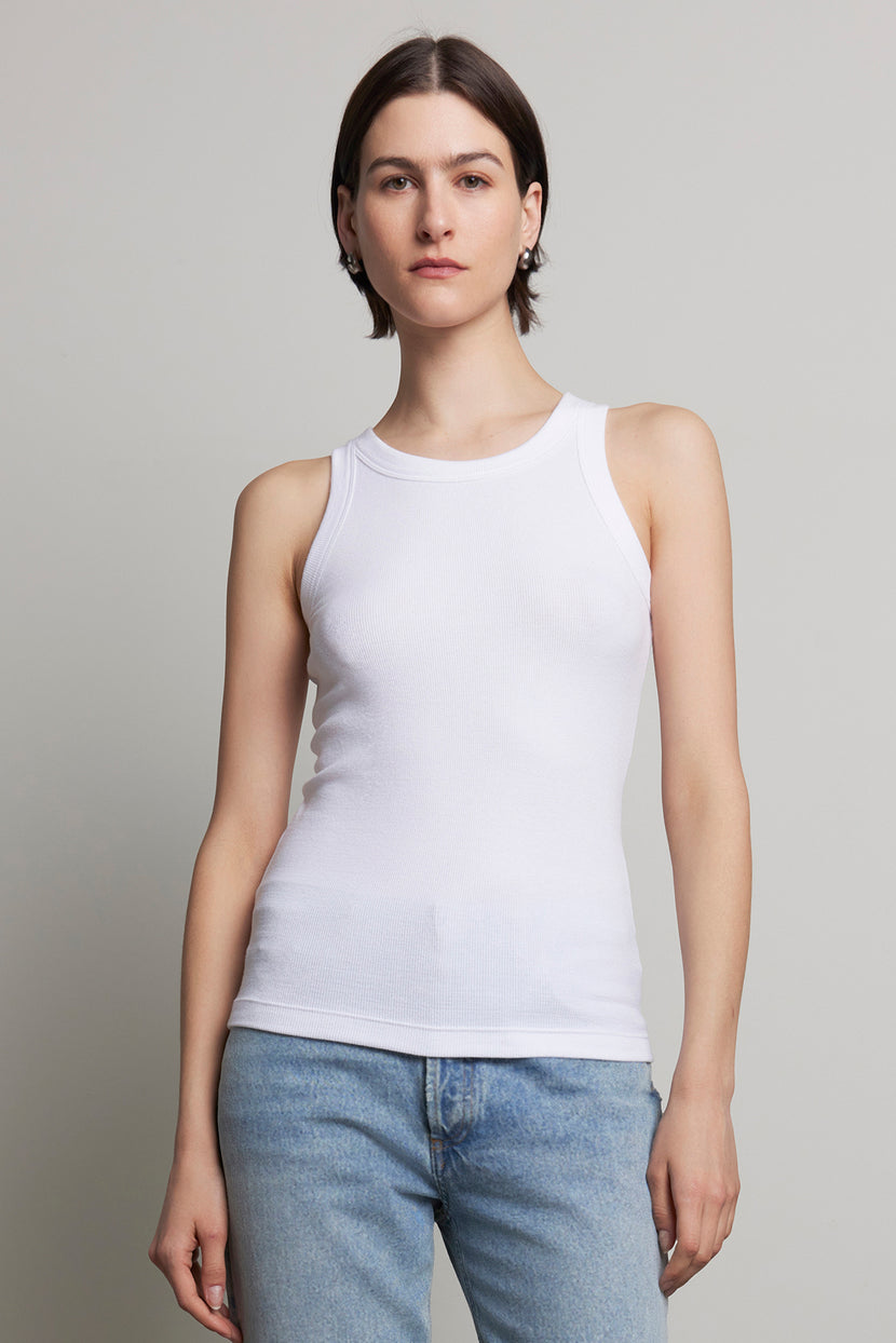 A person with short hair wearing the CRUZ TANK TOP by Velvet by Jenny Graham, crafted from ribbed cotton-modal, and blue jeans stands against a plain background, embodying the essence of a capsule wardrobe.