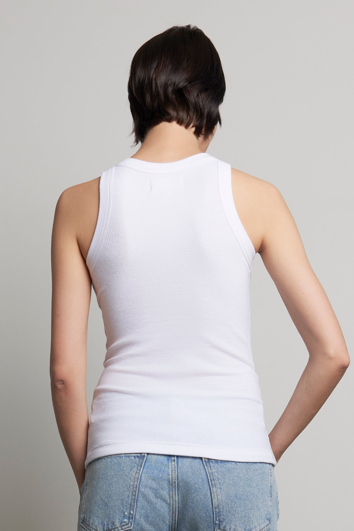 Rear view of a person with short hair wearing the CRUZ TANK TOP by Velvet by Jenny Graham, paired with blue jeans, highlighting a capsule wardrobe essential against a plain background.-38318609334465