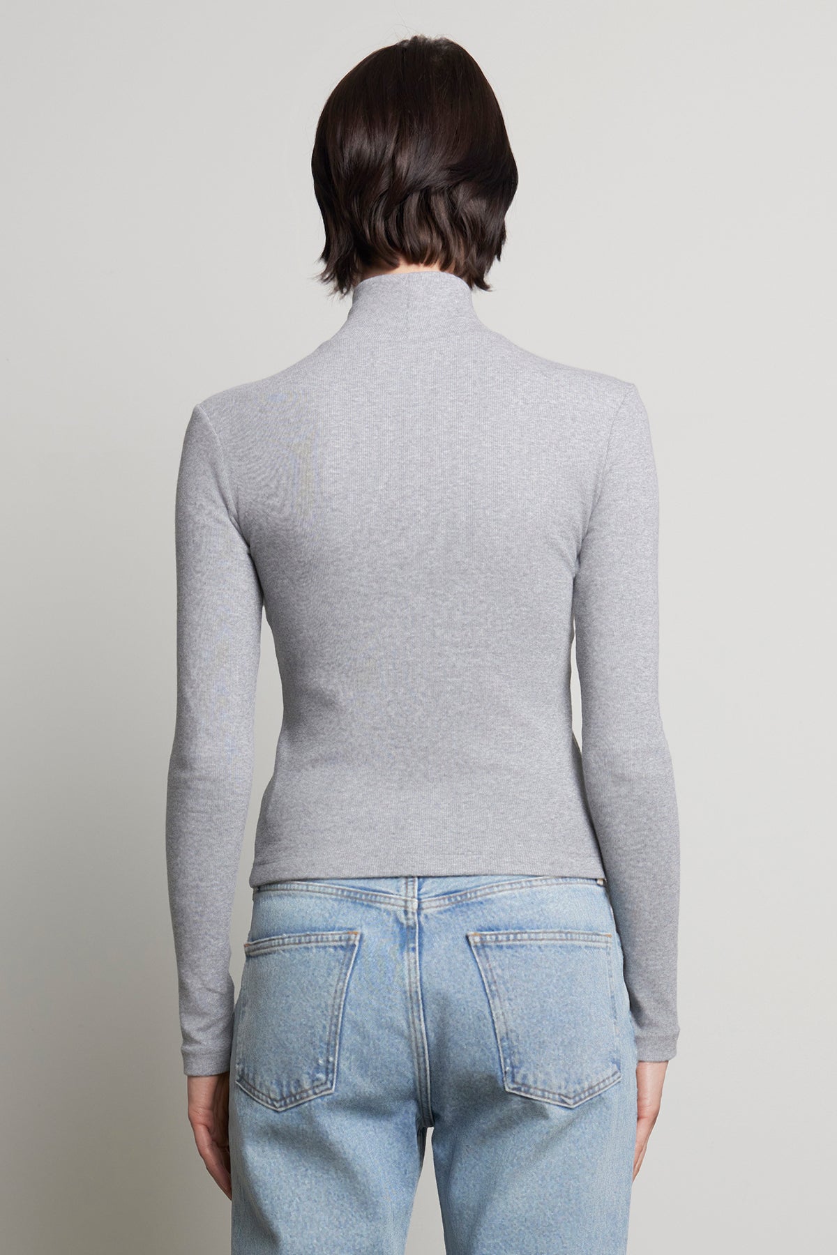   A person with short brown hair is wearing the HELMS TEE by Velvet by Jenny Graham in gray with a ribbed texture turtleneck and paired with light blue jeans, shown from the back. 