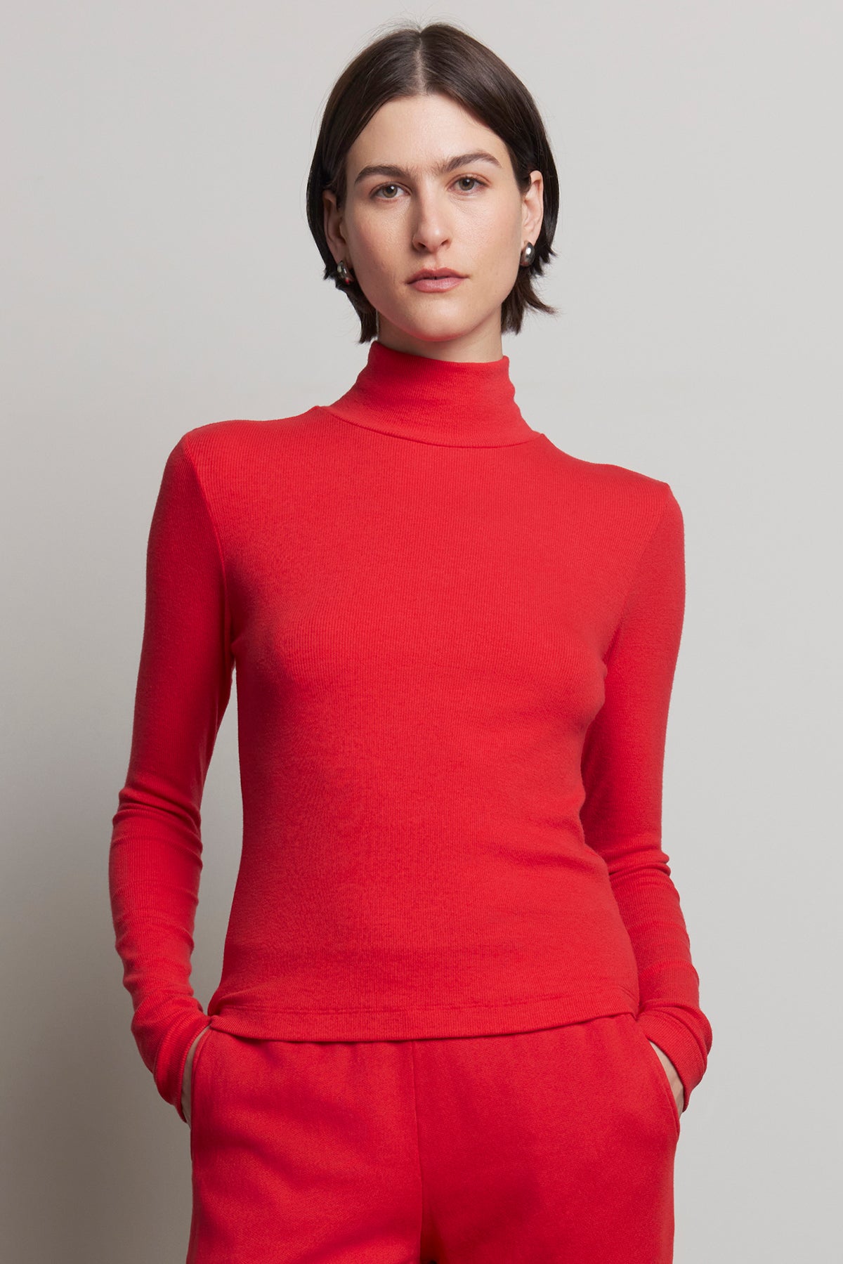 Person wearing the Velvet by Jenny Graham HELMS TEE in red, featuring a mock neck and ribbed texture, paired with matching red pants, stands against a neutral background.-38318597013697