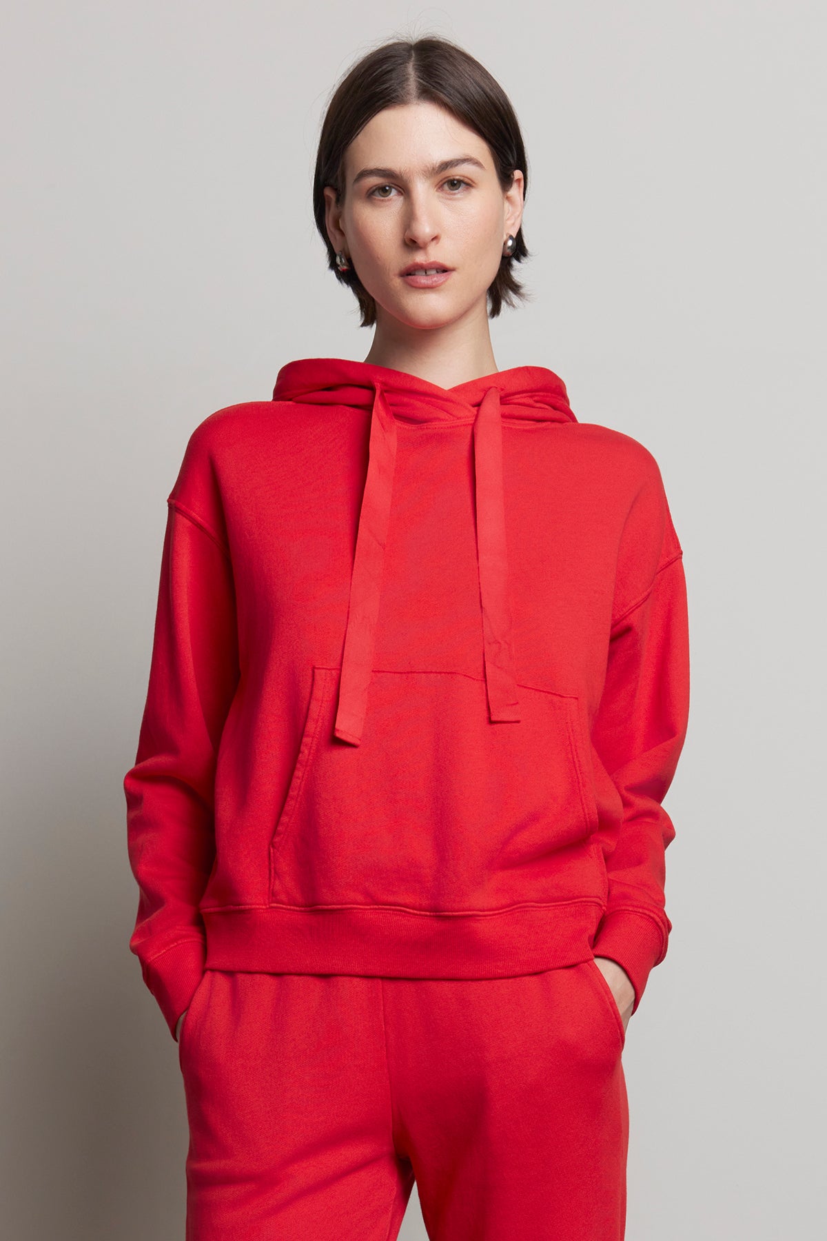   A person wearing an OJAI HOODIE from Velvet by Jenny Graham, made of organic cotton in red, along with matching pants, stands against a plain background. 