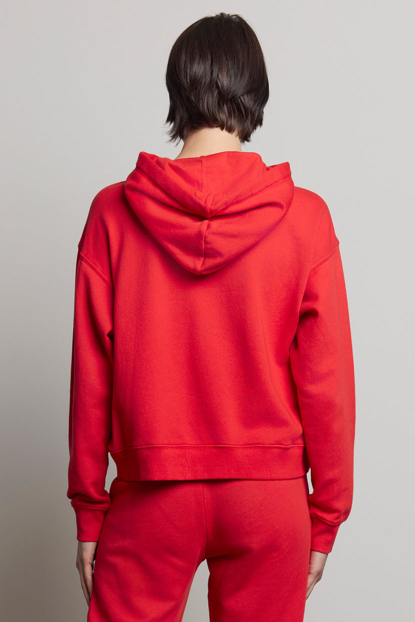 A person is wearing the OJAI HOODIE in a classic red shade, crafted from organic cotton by Velvet by Jenny Graham, paired with matching pants, as they face away.