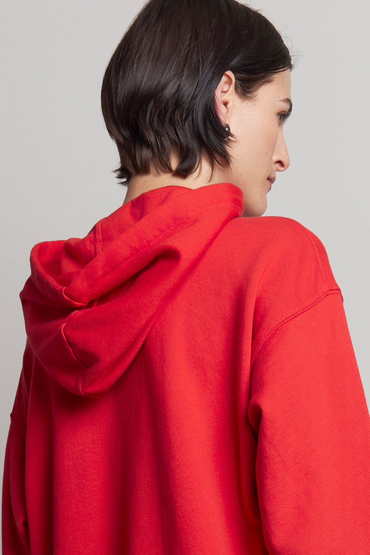   An individual wearing the OJAI HOODIE by Velvet by Jenny Graham, facing away to reveal the back and side profile against a neutral backdrop. 