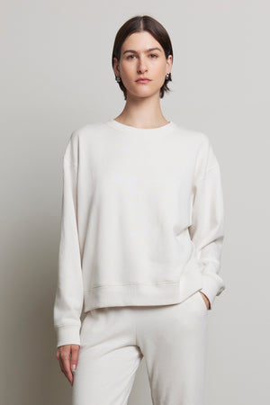 A person wearing the YNEZ SWEATSHIRT and pants from Velvet by Jenny Graham, crafted from organic cotton, stands against a plain background, looking at the camera.