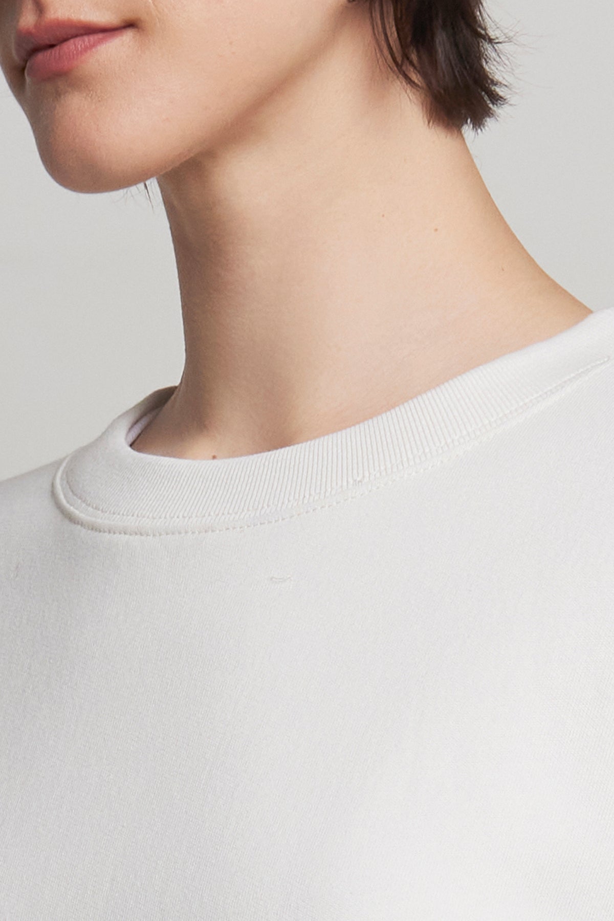   Close-up of an individual dressed in a plain white YNEZ SWEATSHIRT from Velvet by Jenny Graham, crafted from organic cotton. Only the lower half of the face and neck can be seen. 