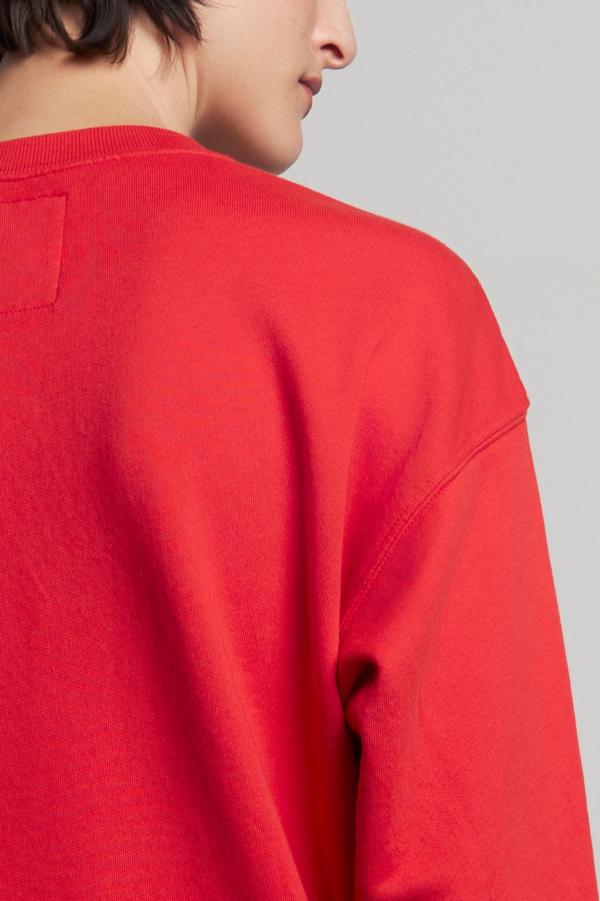   A person wearing the YNEZ SWEATSHIRT from Velvet by Jenny Graham, crafted from organic cotton and in a vibrant red color, is shown from the back with their head turned slightly to the side. 