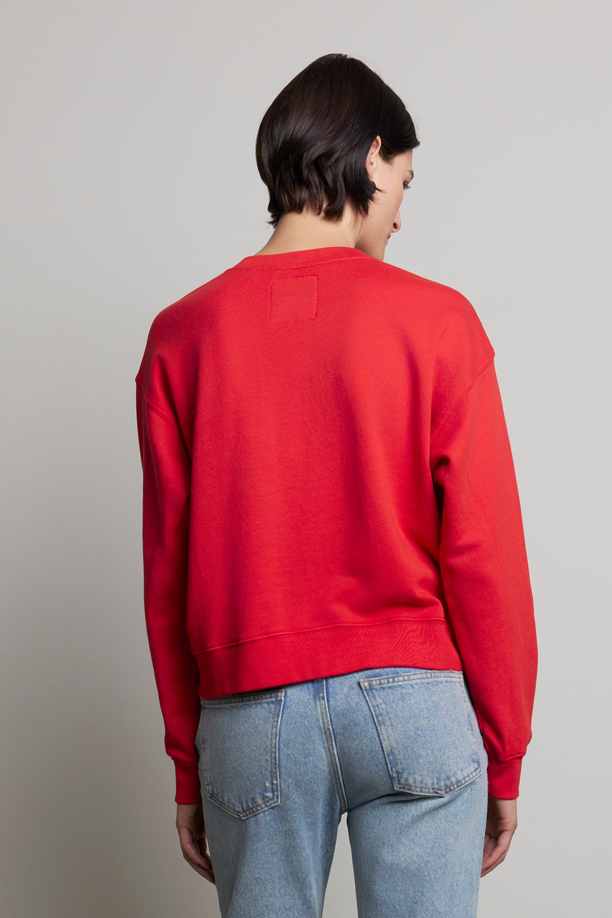   A person wearing the YNEZ SWEATSHIRT by Velvet by Jenny Graham, made of organic cotton in red, and blue jeans is shown from the back against a plain background. 