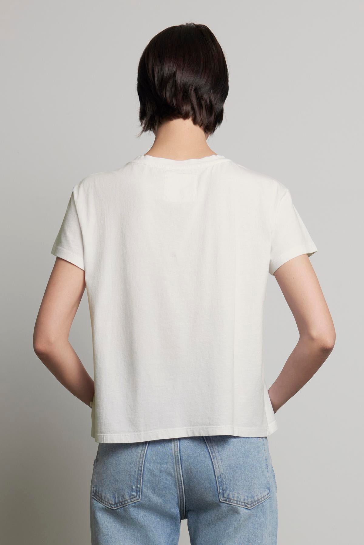   A person with short dark hair is shown from the back, wearing a plain white TOPANGA TEE from Velvet by Jenny Graham and blue jeans. 