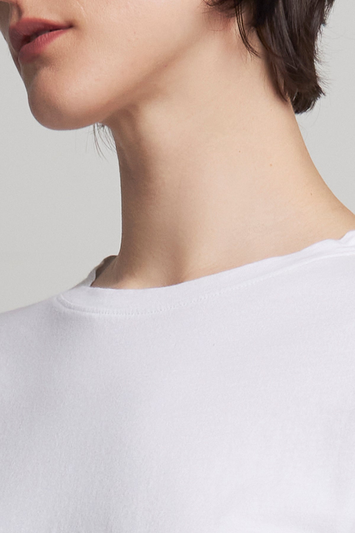   A person in a relaxed fit, white VICENTE TEE by Velvet by Jenny Graham, made of organic cotton, stands showing their short, dark hair from a sideways angle. 