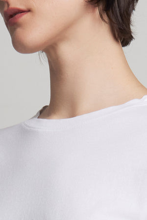 A person in a relaxed fit, white VICENTE TEE by Velvet by Jenny Graham, made of organic cotton, stands showing their short, dark hair from a sideways angle.