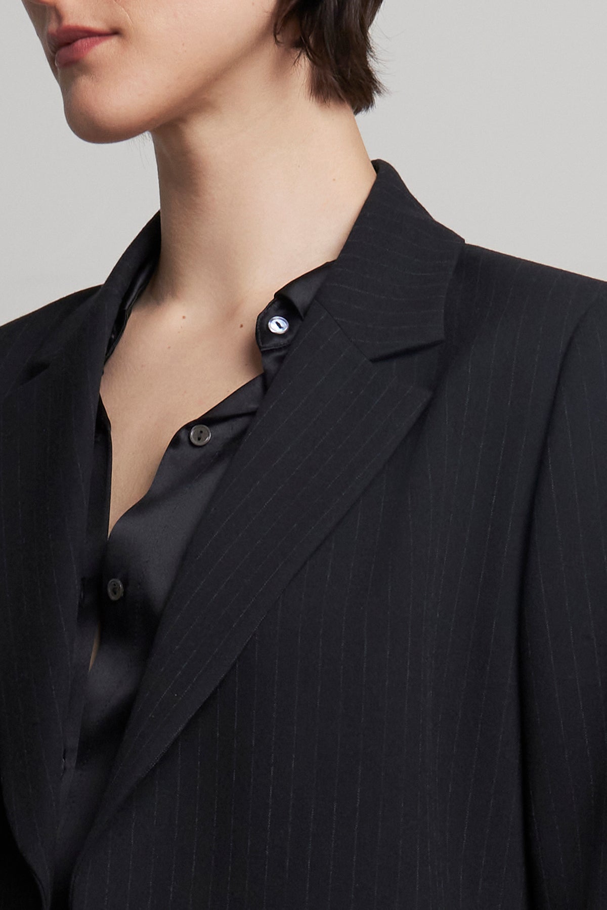 The individual is depicted from the chest up, dressed in a pinstripe polyester ensemble featuring a partially unbuttoned black shirt and the oversized FRESNO PINSTRIPE BLAZER by Velvet by Jenny Graham. The notched collar adds a sharp touch to the look.-38318584070337