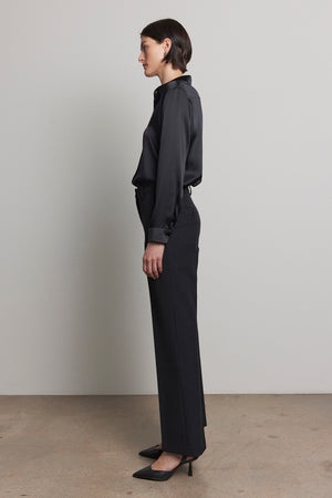 A person standing in profile, wearing a dark long-sleeved shirt paired with the TAHOE PINSTRIPE PANT by Velvet by Jenny Graham and complemented by black heels, against a neutral background.