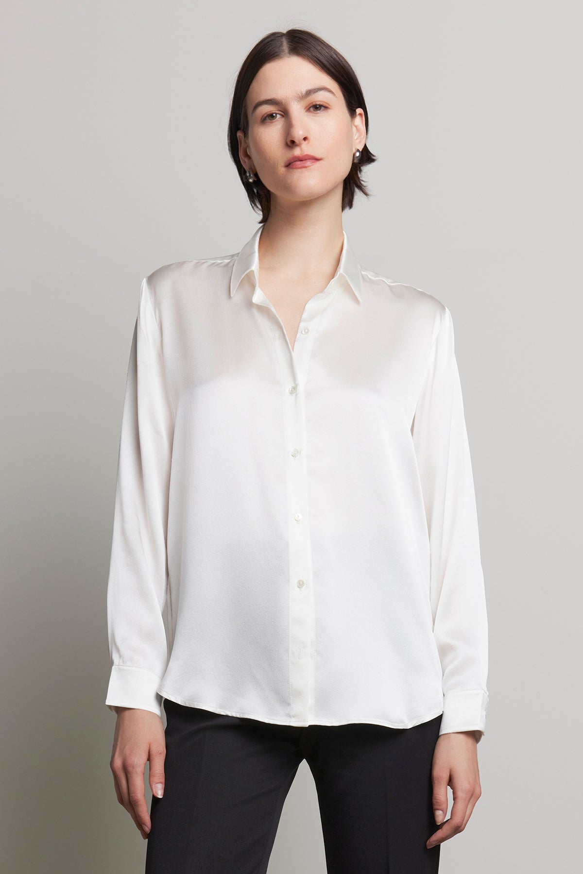   A person wearing the CALABASAS SILK CHARMEUSE BLOUSE by Velvet by Jenny Graham, paired with black pants, stands against a plain background, showcasing an elegant drape. 