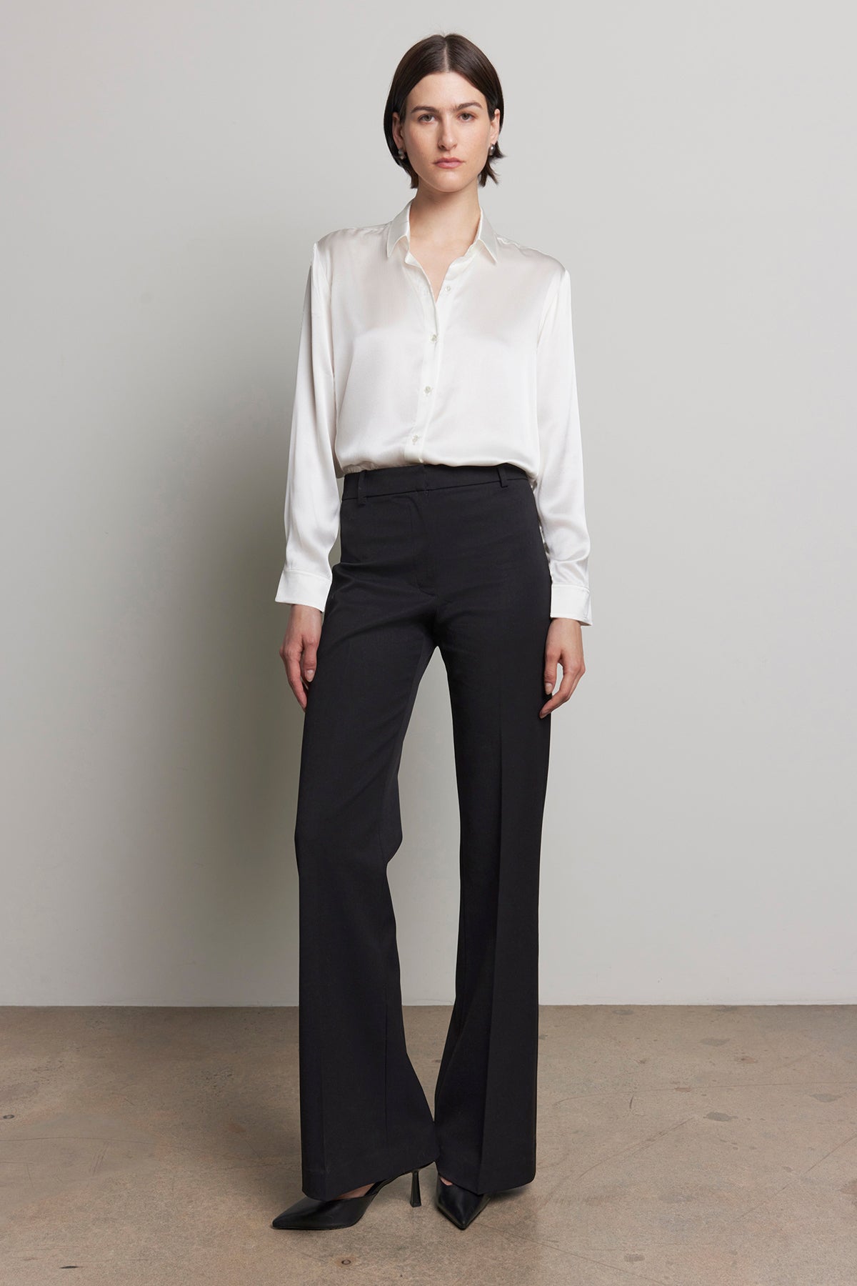 Against a plain background, a person is standing in the MARIPOSA PANT by Velvet by Jenny Graham, featuring a white blouse and black, soft suiting fabric with flared legs.-38318589870273