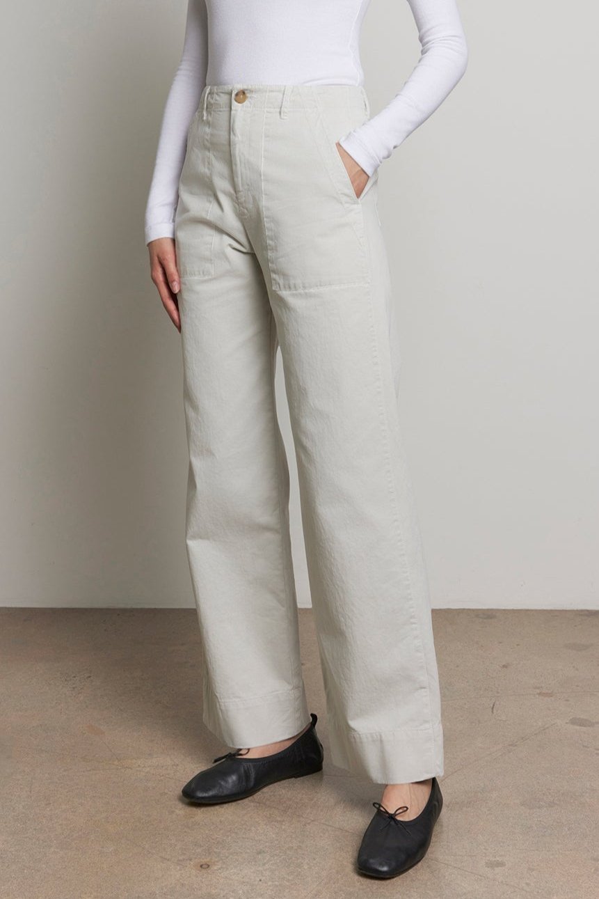   A person stands against a neutral background wearing a white turtleneck, the light-colored VENTURA PANT by Velvet by Jenny Graham, and black shoes. 