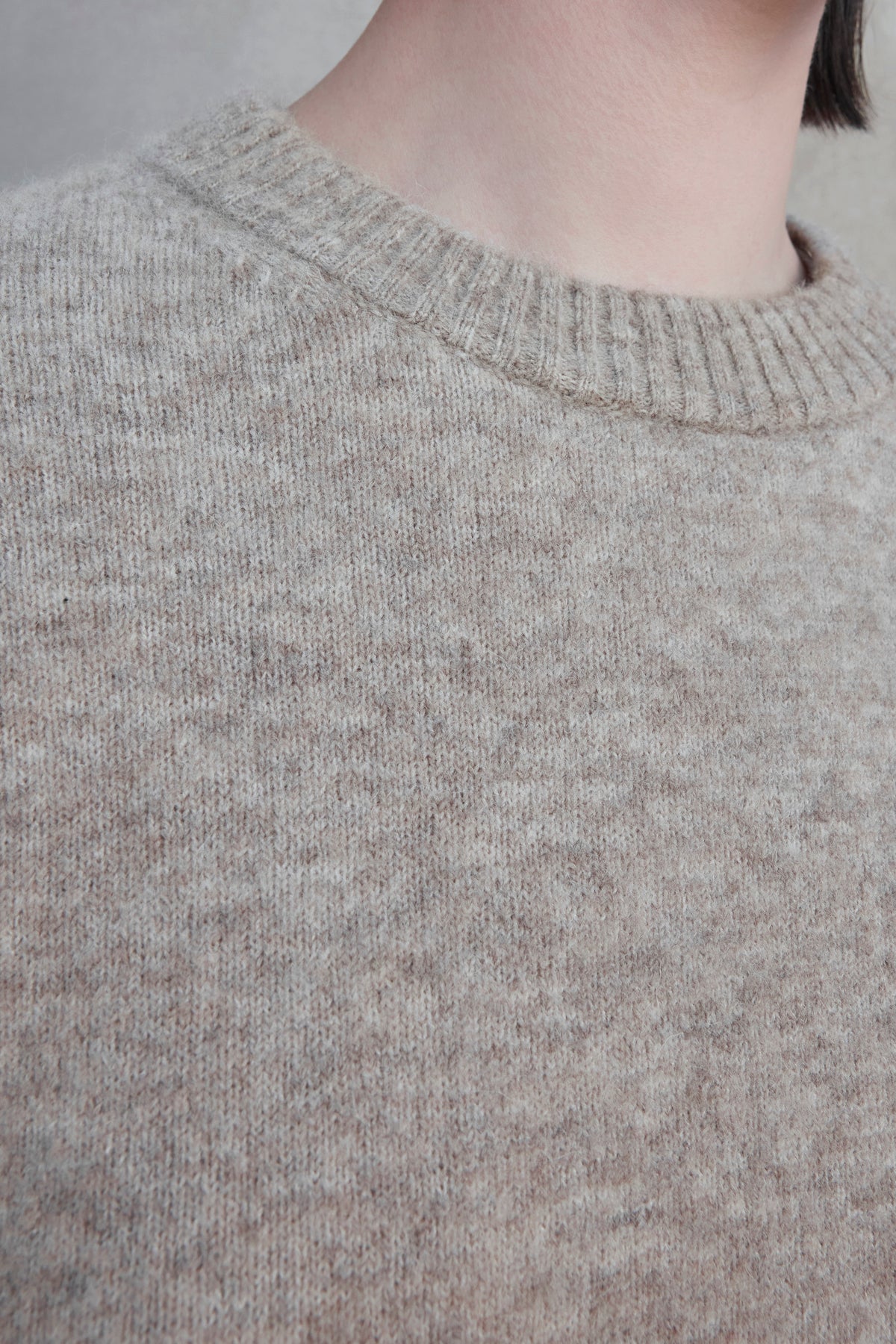   Close-up of a person wearing the LAKEWOOD ALPACA SWEATER by Velvet by Jenny Graham, featuring a light brown woolen texture with a crew neckline. 