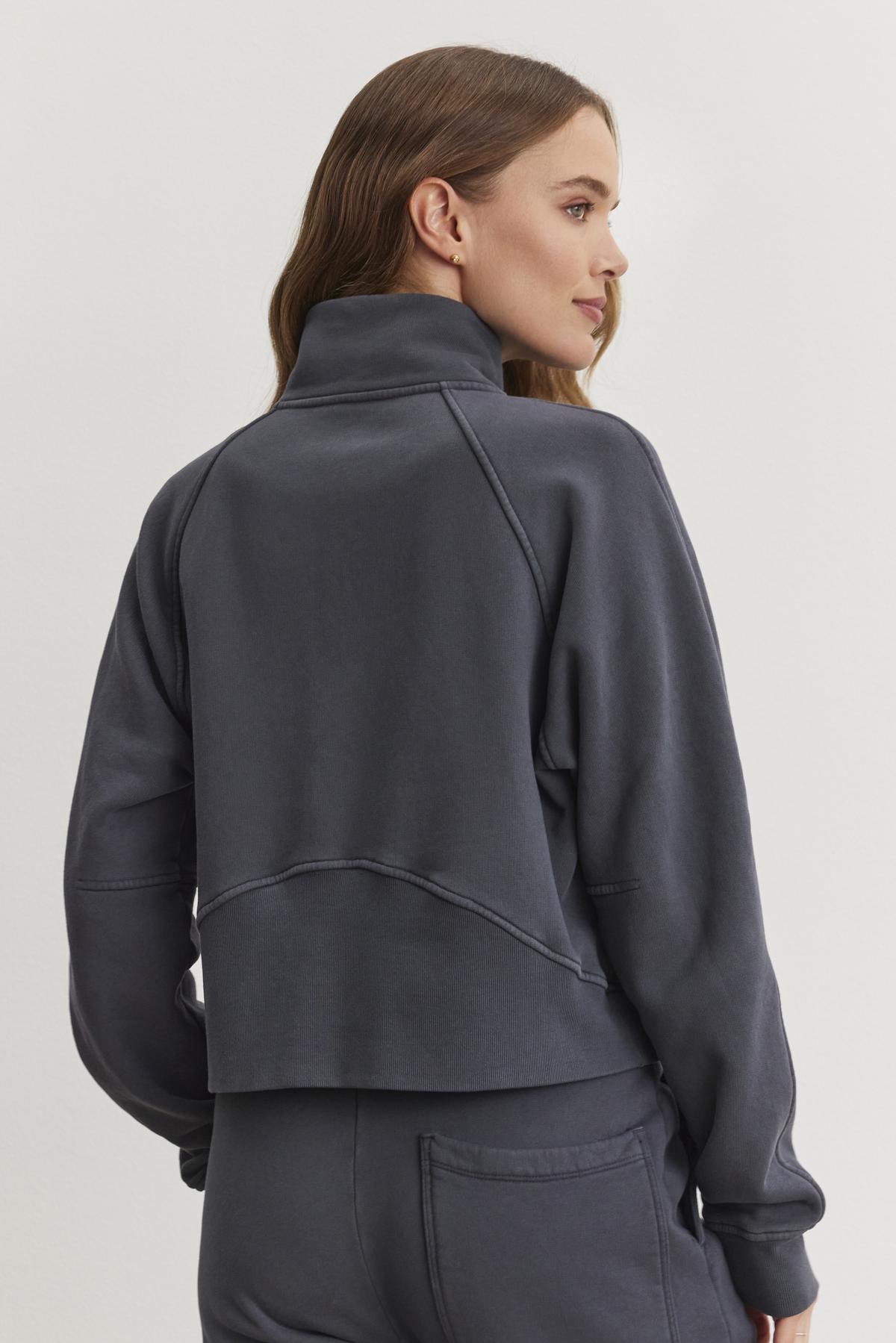   A person wearing a cozy Velvet by Graham & Spencer dark gray high-neck Cecilia Full-Zip Jacket paired with matching pants is turned slightly to the side, looking off-camera against a plain light background. 