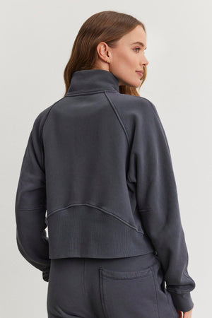 A person wearing a cozy Velvet by Graham & Spencer dark gray high-neck Cecilia Full-Zip Jacket paired with matching pants is turned slightly to the side, looking off-camera against a plain light background.