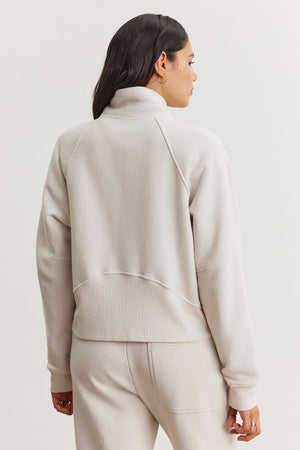 A woman is wearing the Velvet by Graham & Spencer CECILIA FULL-ZIP JACKET, a cozy essential in light gray cotton fleece with raglan sleeves, accompanied by matching pants, as she faces away on a plain background.