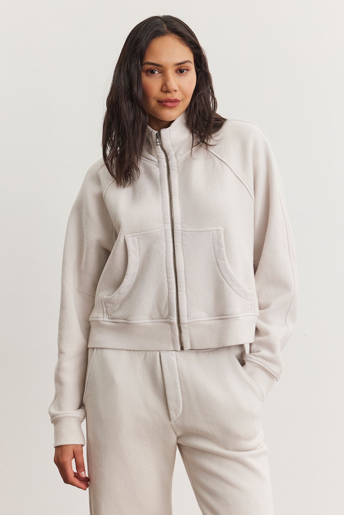 A person wearing a CECILIA FULL-ZIP JACKET by Velvet by Graham & Spencer, featuring light gray cotton fleece and raglan sleeves, with matching pants stands against a plain background.-38301296361665