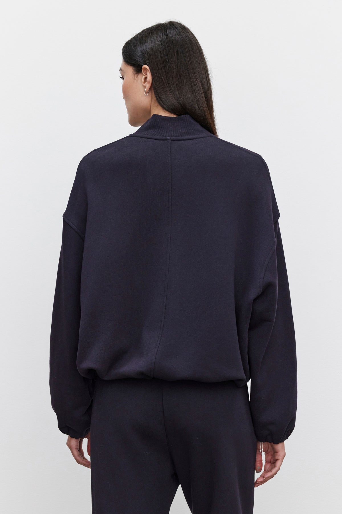 Rear view of a person wearing an oversized fit, long-sleeved GENEVIEVE ZIP-UP SWEATSHIRT by Velvet by Graham & Spencer and matching pants. The sweatshirt is made of heavier-weight cotton fleece. The person has long, dark hair.-37856522993857