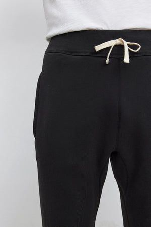 Person wearing KENJI SWEATPANT by Velvet by Graham & Spencer in black with white drawstrings and a white t-shirt, showcasing a comfortable fit.