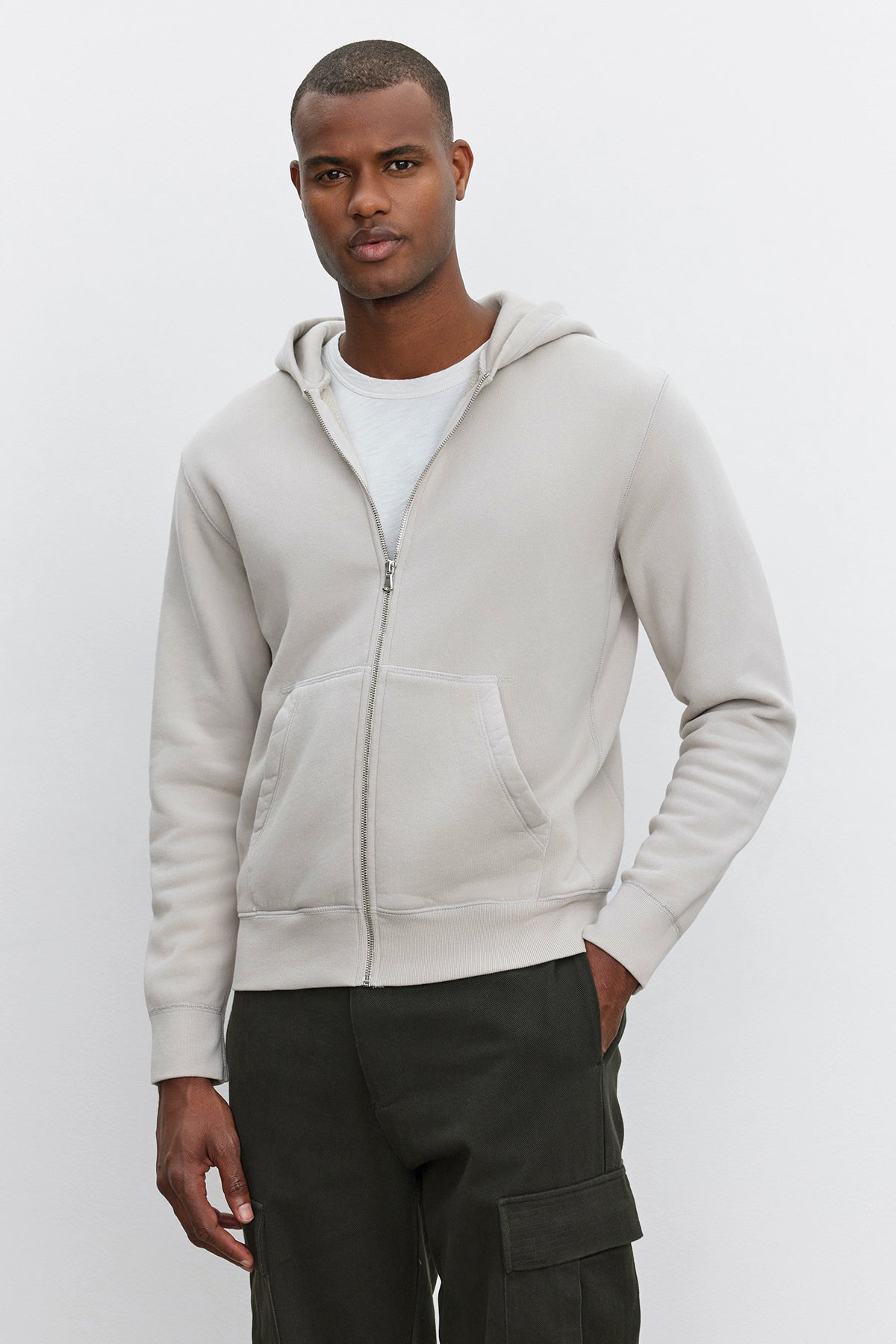   A man wearing the Velvet by Graham & Spencer REN HOODIE in light grey and dark green vintage-style pants stands against a plain white background. 