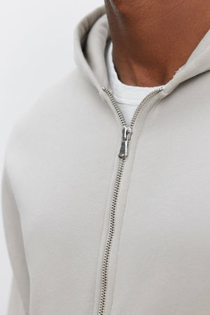 Close-up of a person wearing the REN HOODIE from Velvet by Graham & Spencer, a light gray, cotton fleece, full-zip hoodie over a white t-shirt, focusing on the zipper and chest area.